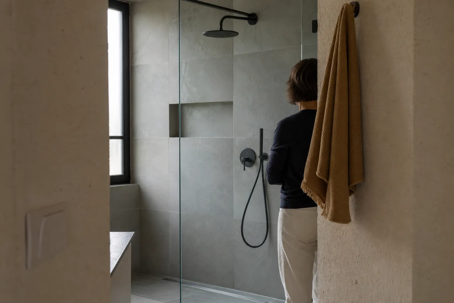 Douche de plain-pied achevée dans une petite salle d'eau, grand carrelage gris et paroi vitrée