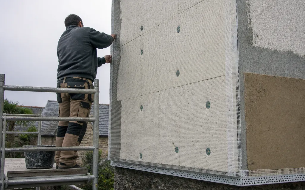 Chantier d'isolation par l'extérieur, panneaux fixés sur la façade et rail de départ visible en pied de mur